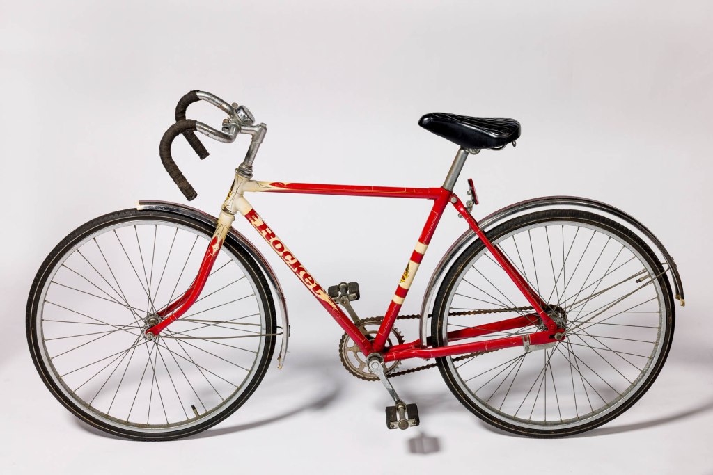 A vintage 'Rocket' bicycle, featuring a steel frame painted in Royal Red with decorative elements in Pale Ivory, showcasing its single-speed design and classic bike handlebars.