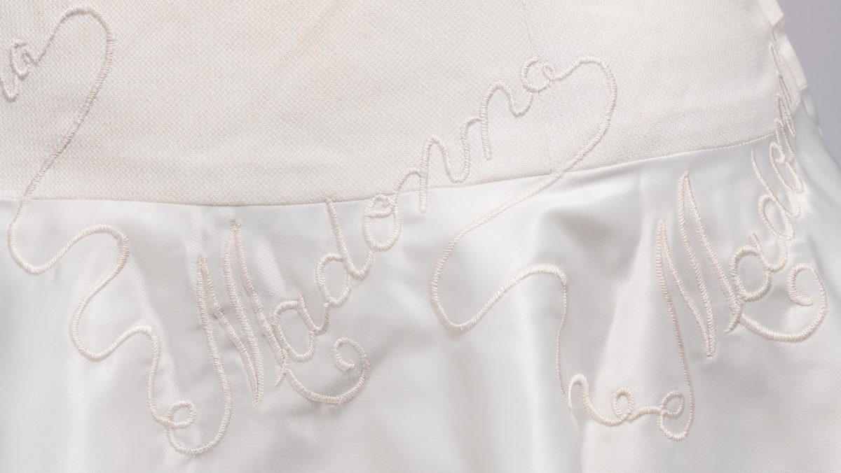 White cotton pique tennis dress consisting of a flared silk-satin, satin-lined skirt attached to a fitted bodice shaped by double-ended darts at front and standard darts at back, front crew neckline, scooped back neckline. Was worn at Wimbledon in the 1960s by Queensland tennis player and member of the 1962 Australian Women's Tennis Team, Madonna Schacht.