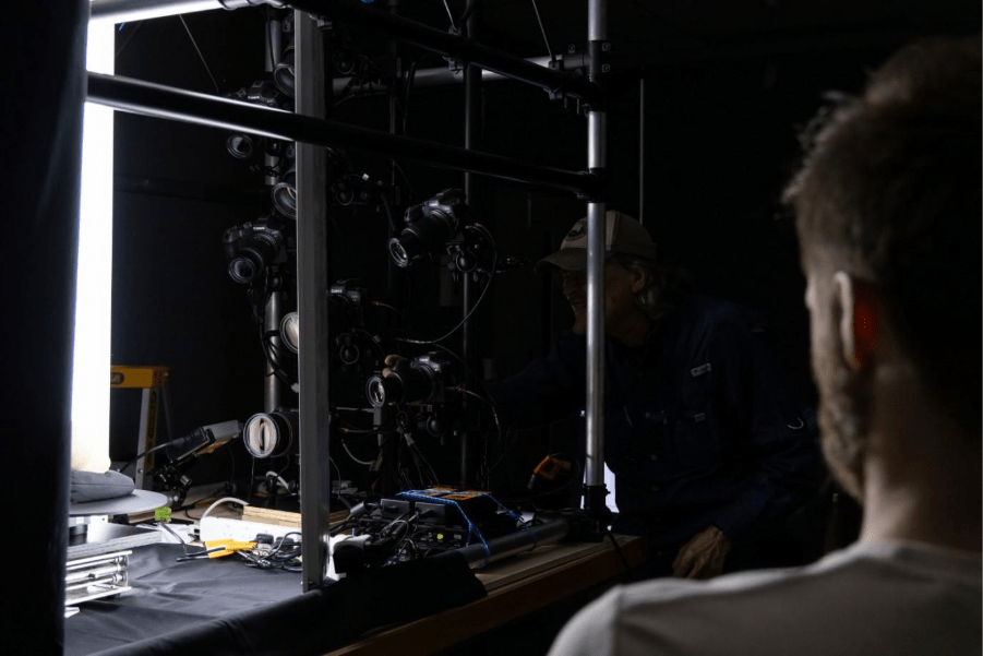 A person adjusting camera equipment in a dark studio, with multiple cameras set up for a photoshoot.
